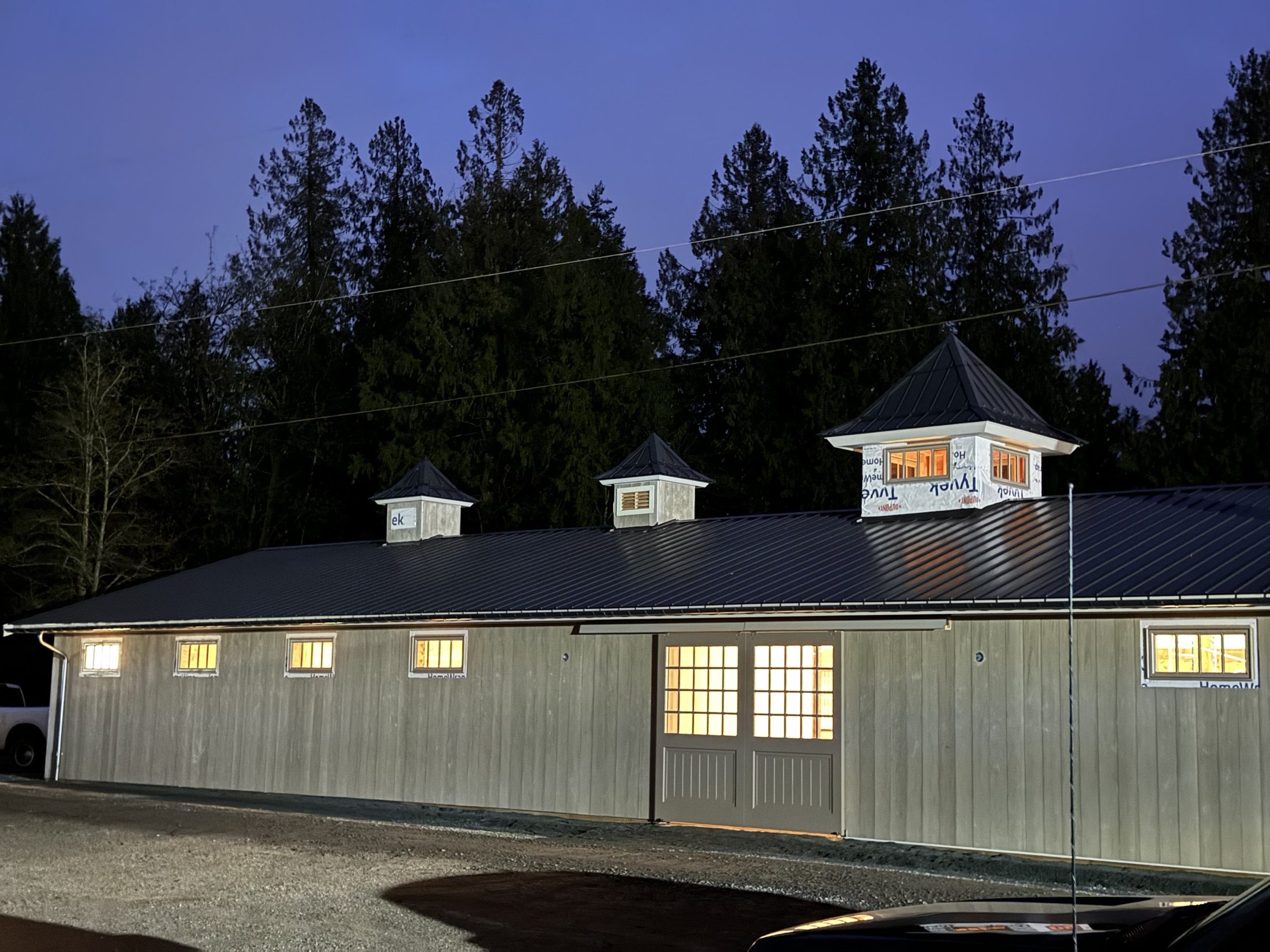 Coast Performance Horses riding arena and barn, Langley — finished equestrian barn at dusk with three lantern-roof cupolas glowing