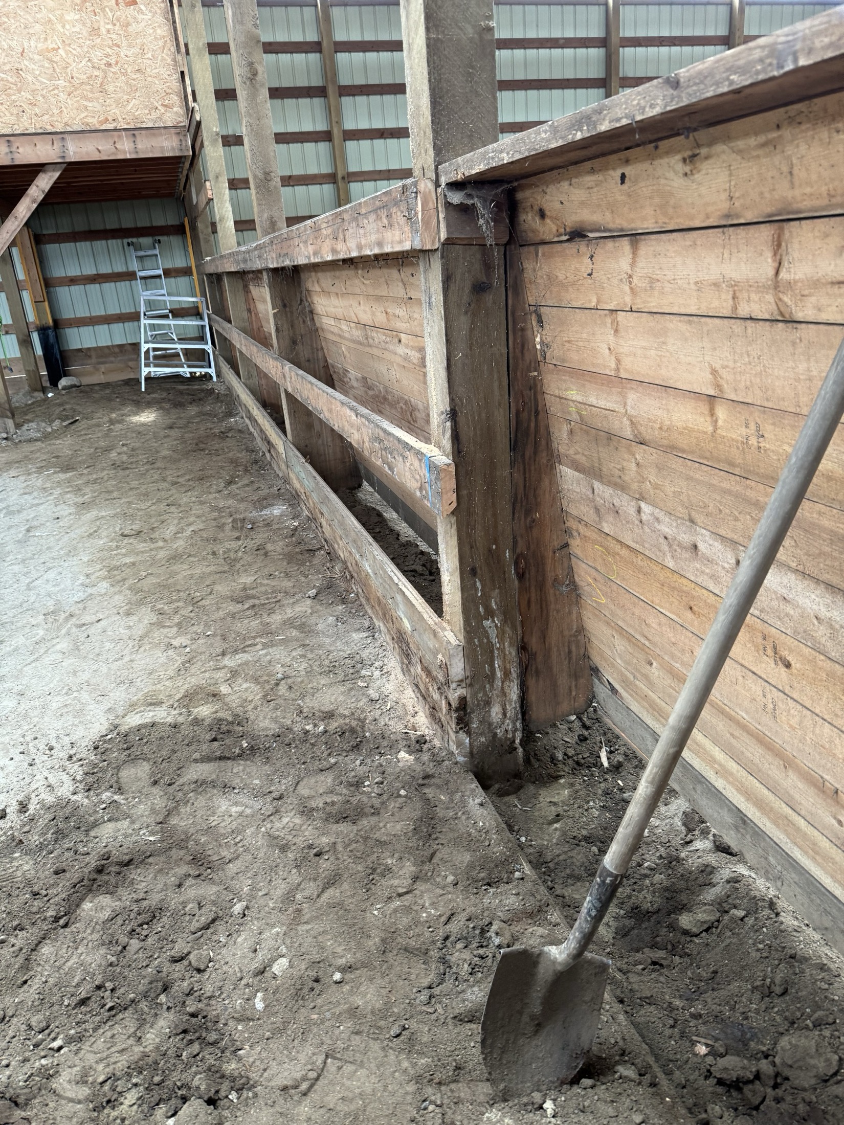 Wide view of the original kick rail and wall at Coast Performance Horses, Langley, before replacement, shovel excavating around a rotten post base