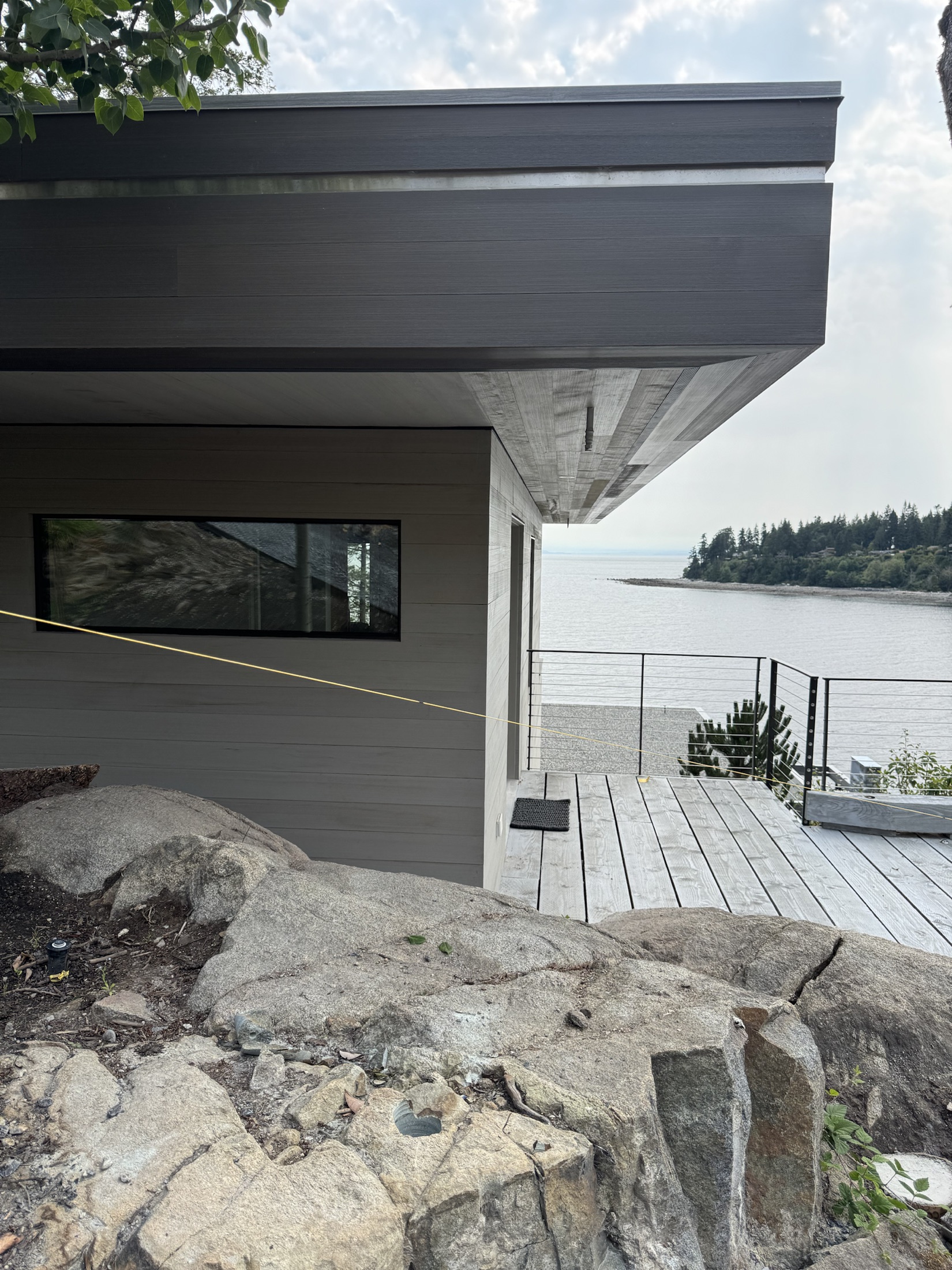 Renova Design Build custom home at Cove Beach, Sechelt — dark cantilevered roofline over finished siding, ocean visible below