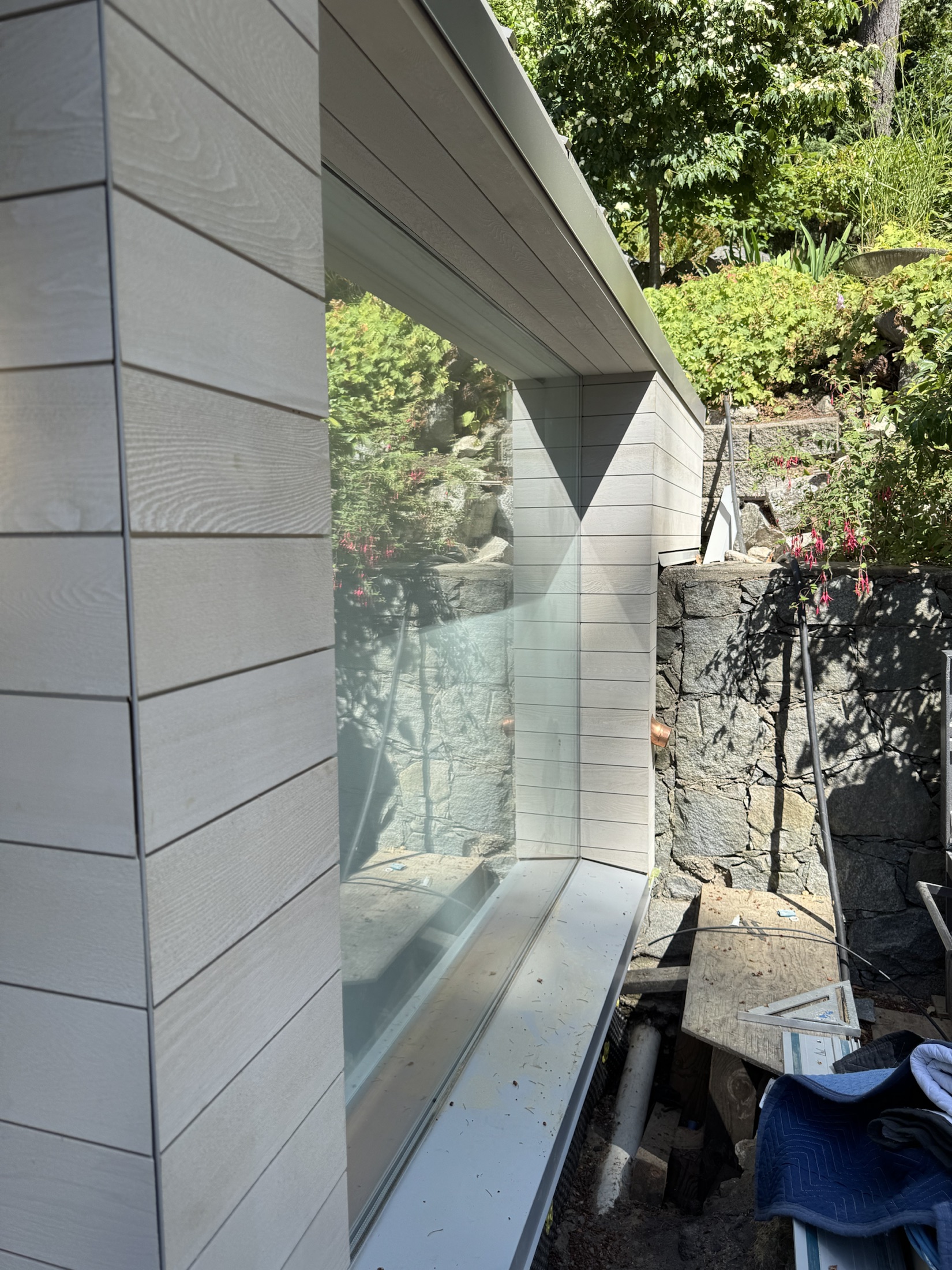 Lawrence Way custom home, West Vancouver — finished cedar cladding alongside an angled window, stone retaining wall and garden behind
