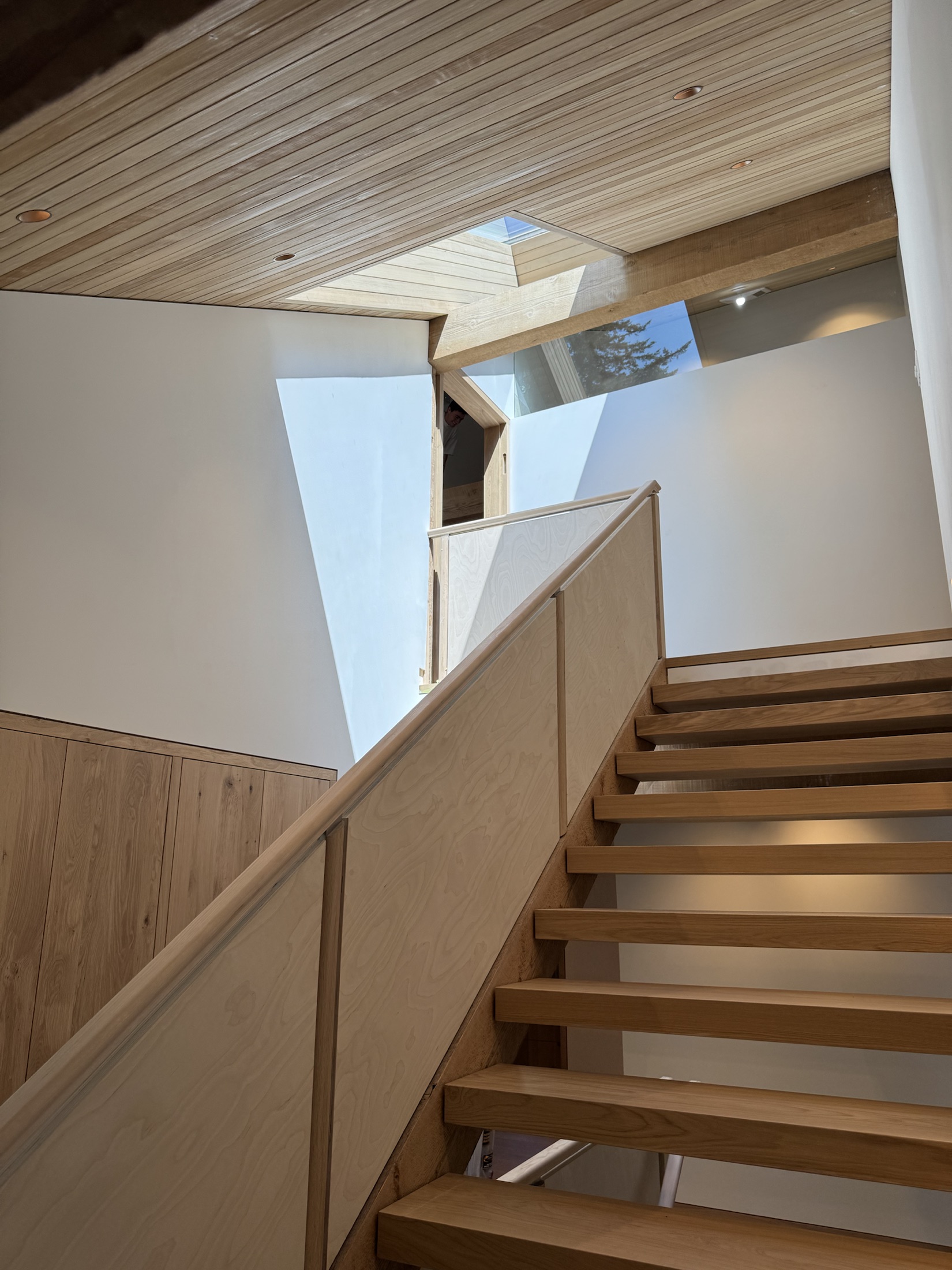 Open-riser oak staircase with a glass railing under a hemlock plank soffit at the Lawrence Way custom home, West Vancouver