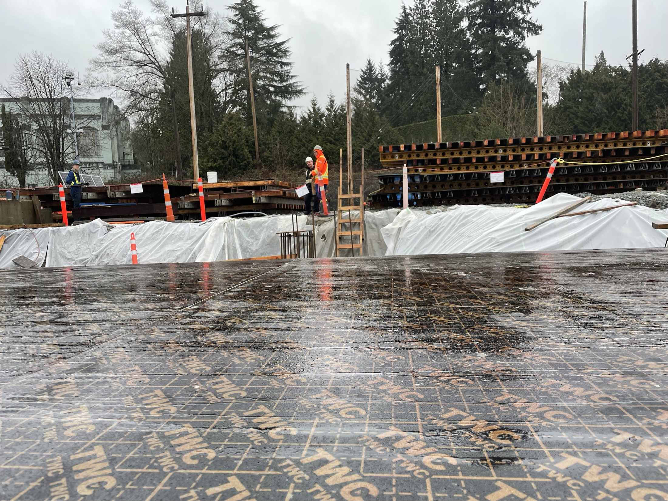 Commercial concrete formwork on an urban job site — crew in full PPE, branded form panels, structural steel and rebar