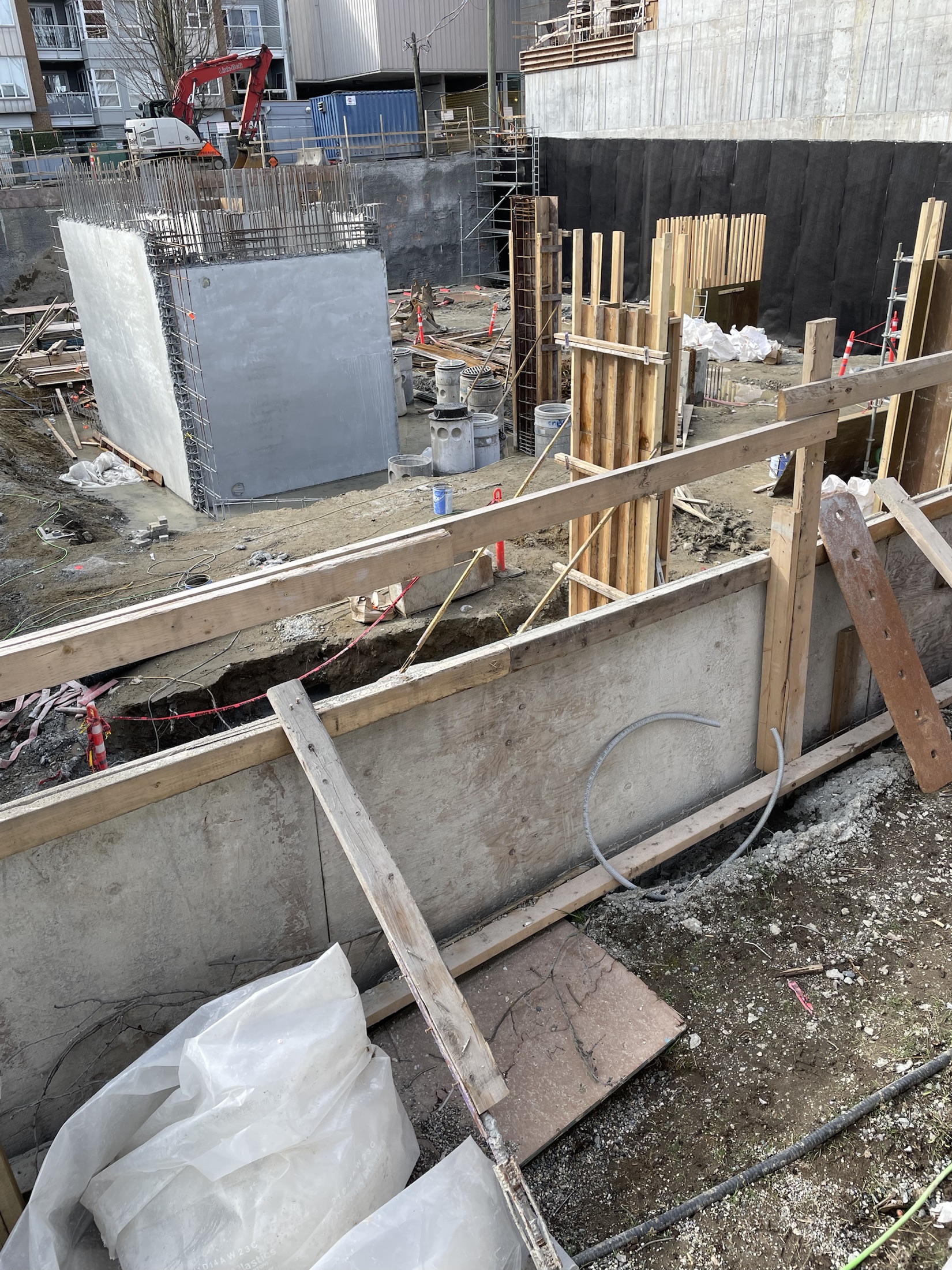Deep excavation with formed foundation walls and column forms on an urban commercial site, excavator working above