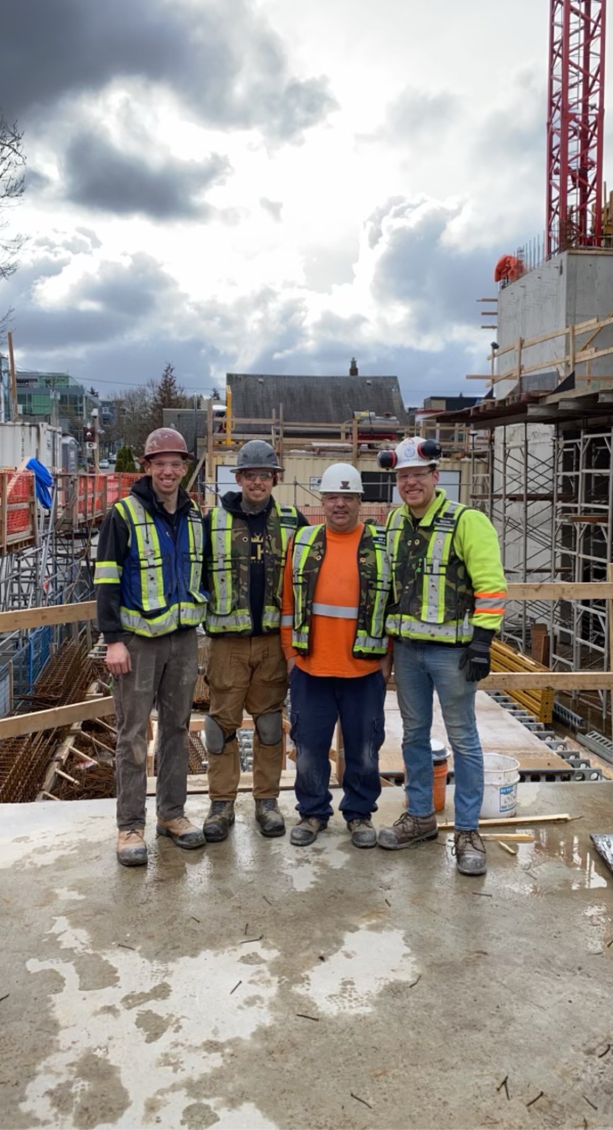 Renova Design Build crew of four in full PPE on a commercial concrete pour in Metro Vancouver, a tower crane rising behind them