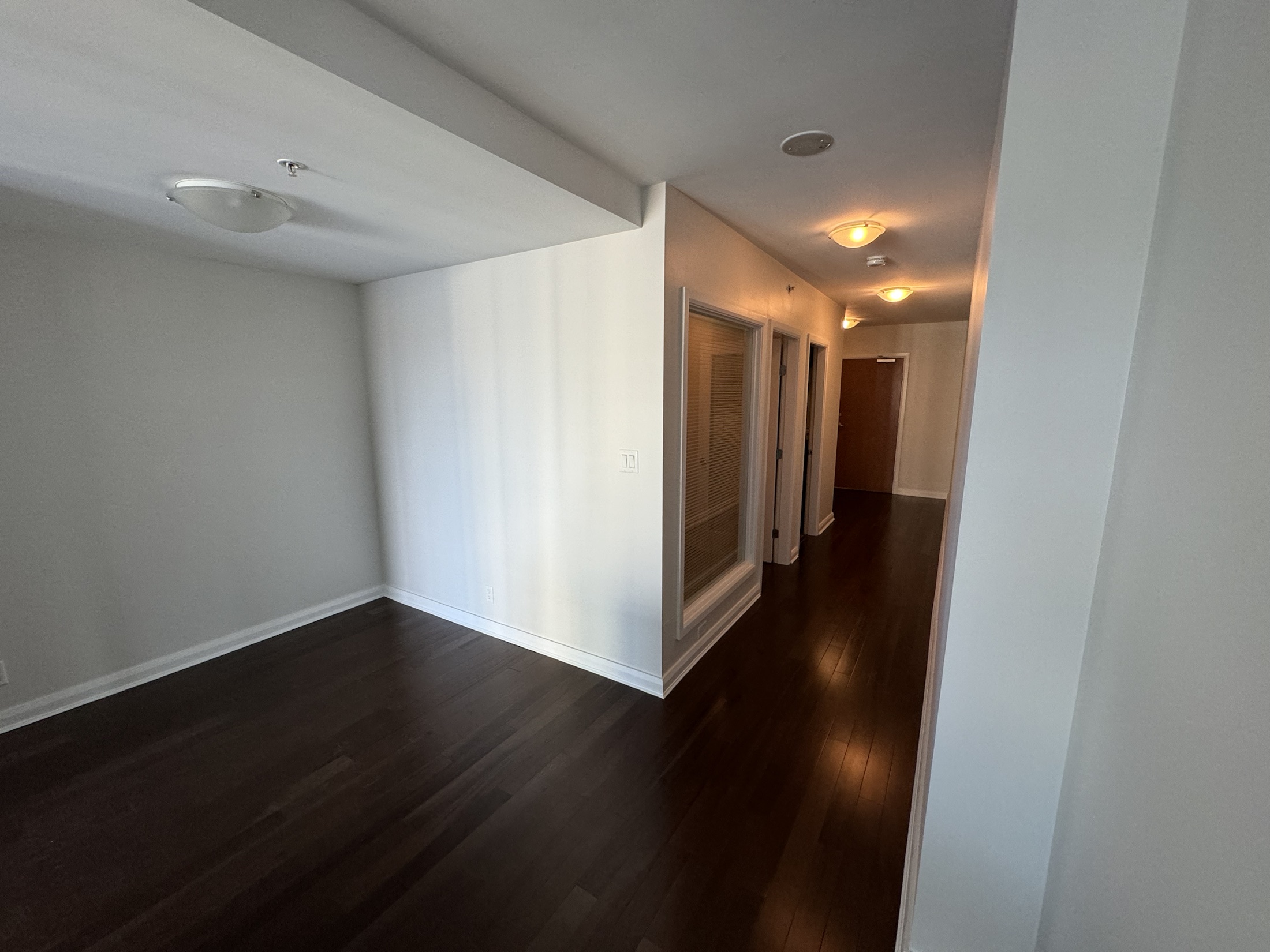 Wende hallway before renovation in New Westminster — dark-stained hardwood flooring and dated ceiling fixtures